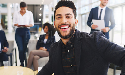 Buy stock photo Cropped portrait of a handsome young businessman sitting and smiling while his colleagues work behind him in the office