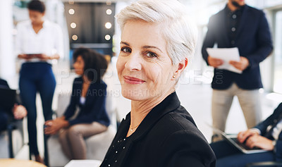 Buy stock photo Cropped portrait of an attractive mature businesswoman sitting and smiling while her colleagues work behind her in the office