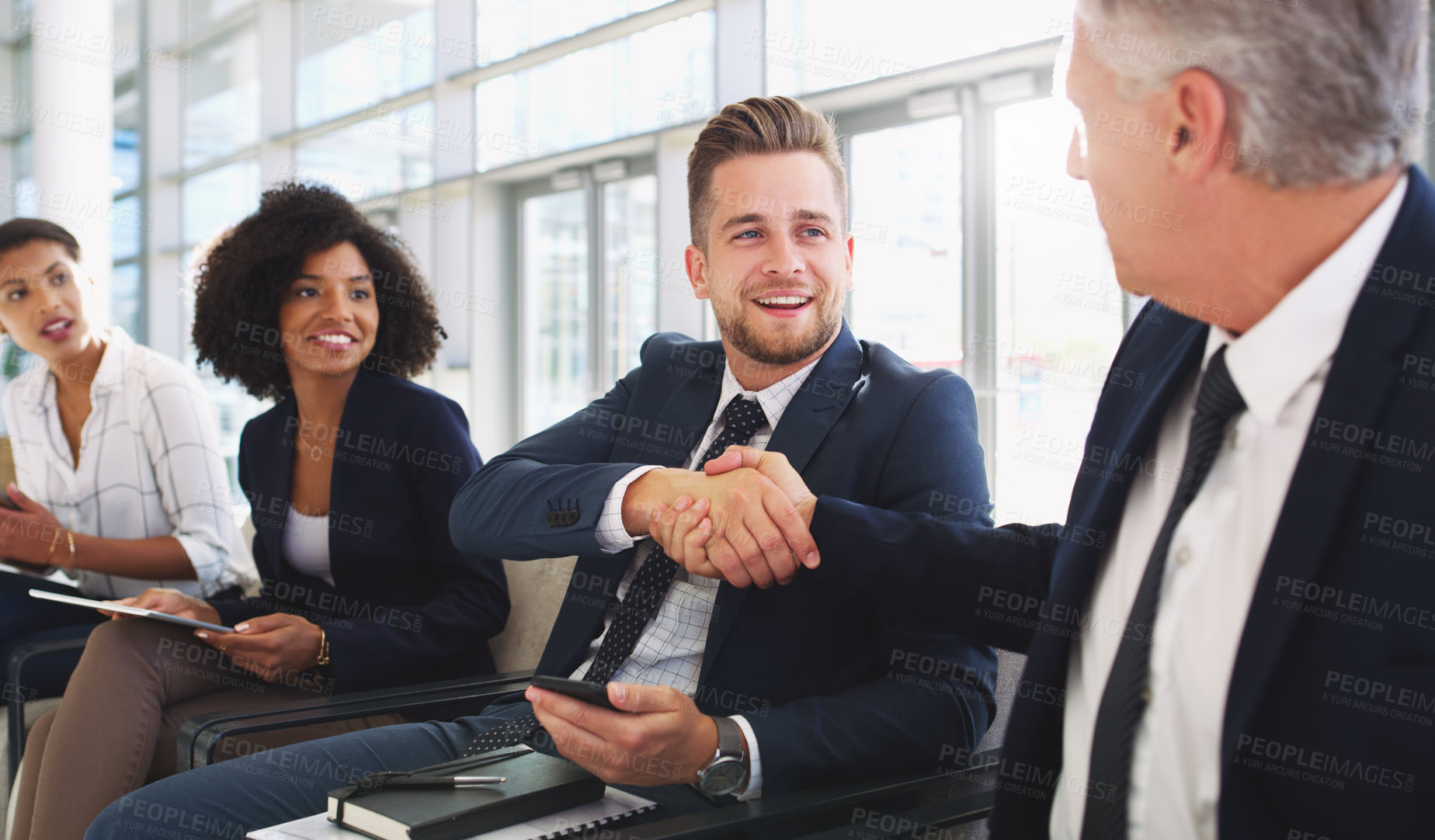 Buy stock photo Cropped shot of a handsome young businessman shaking hands with a colleague while sitting in a line in the office