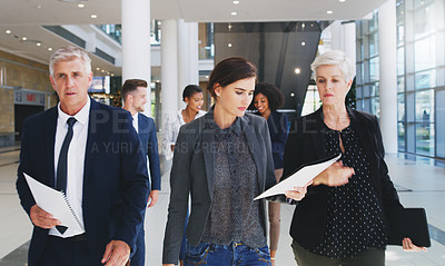 Buy stock photo Cropped shot of a diverse group of businesspeople looking at paperwork and walking through the office during the day