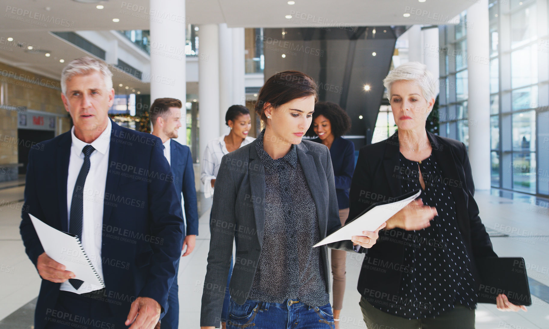 Buy stock photo Cropped shot of a diverse group of businesspeople looking at paperwork and walking through the office during the day
