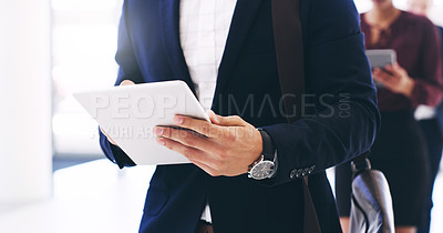 Buy stock photo Cropped shot of an unrecognizable businessman using a tablet while walking through the office during the day