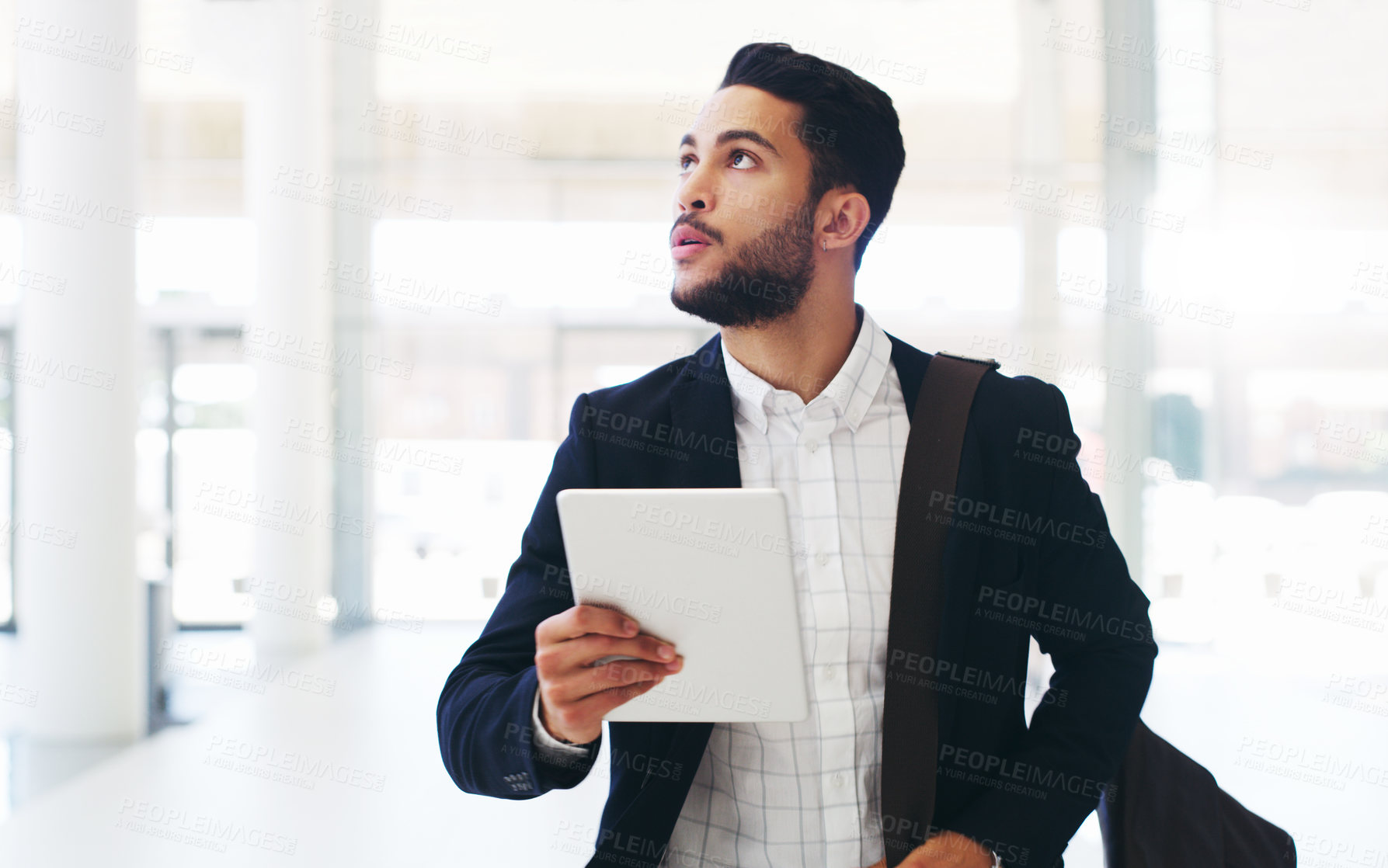 Buy stock photo Cropped shot of a handsome young businessman using a tablet while walking through the office during the day