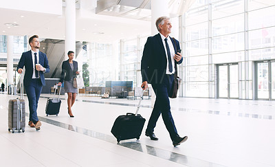 Buy stock photo Full length shot of three businesspeople walking and pulling suitcases while in the office during the day