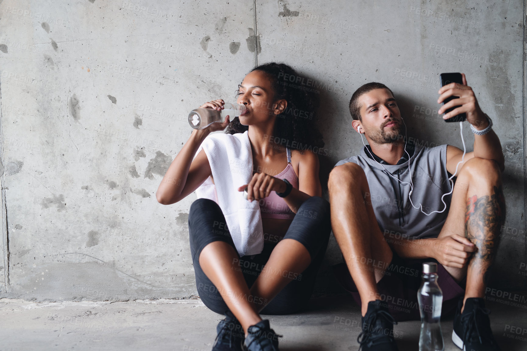 Buy stock photo Shot of a sporty young couple sitting down and taking a break while exercising inside a parking lot