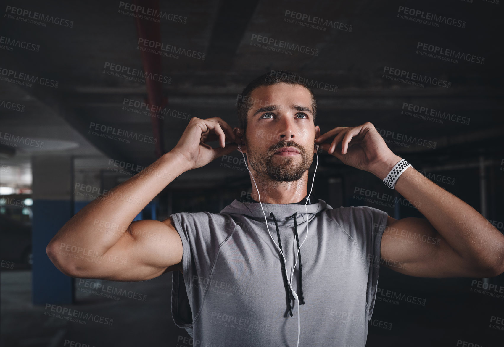 Buy stock photo Shot of a handsome young sportsman listening to music on his earphones while exercising inside a parking lot