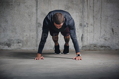 Buy stock photo Shot of a handsome young sportsman doing push ups while exercising inside a parking lot