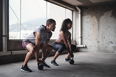 Buy stock photo Full length shot of a sporty young couple exercising with kettlebells inside an underground parking lot