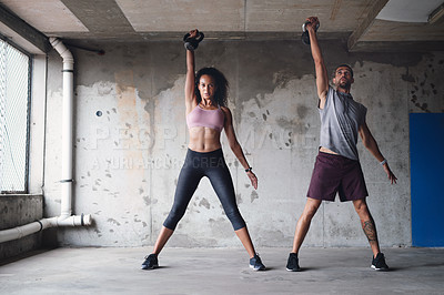Buy stock photo Full length shot of a sporty young couple exercising with kettlebells inside an underground parking lot