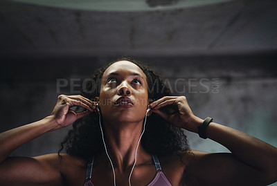 Buy stock photo Shot of an attractive young sportswoman listening to music on her earphones while exercising inside a parking lot