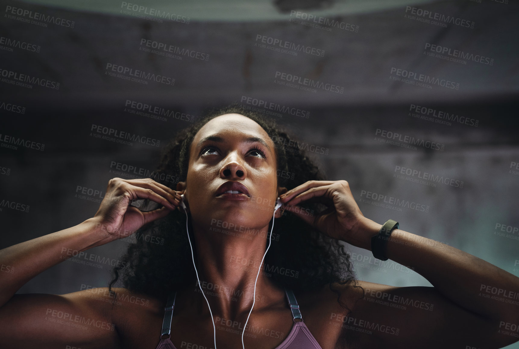 Buy stock photo Shot of an attractive young sportswoman listening to music on her earphones while exercising inside a parking lot
