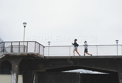 Buy stock photo Full length shot of a sporty young couple running on bridge together outdoors