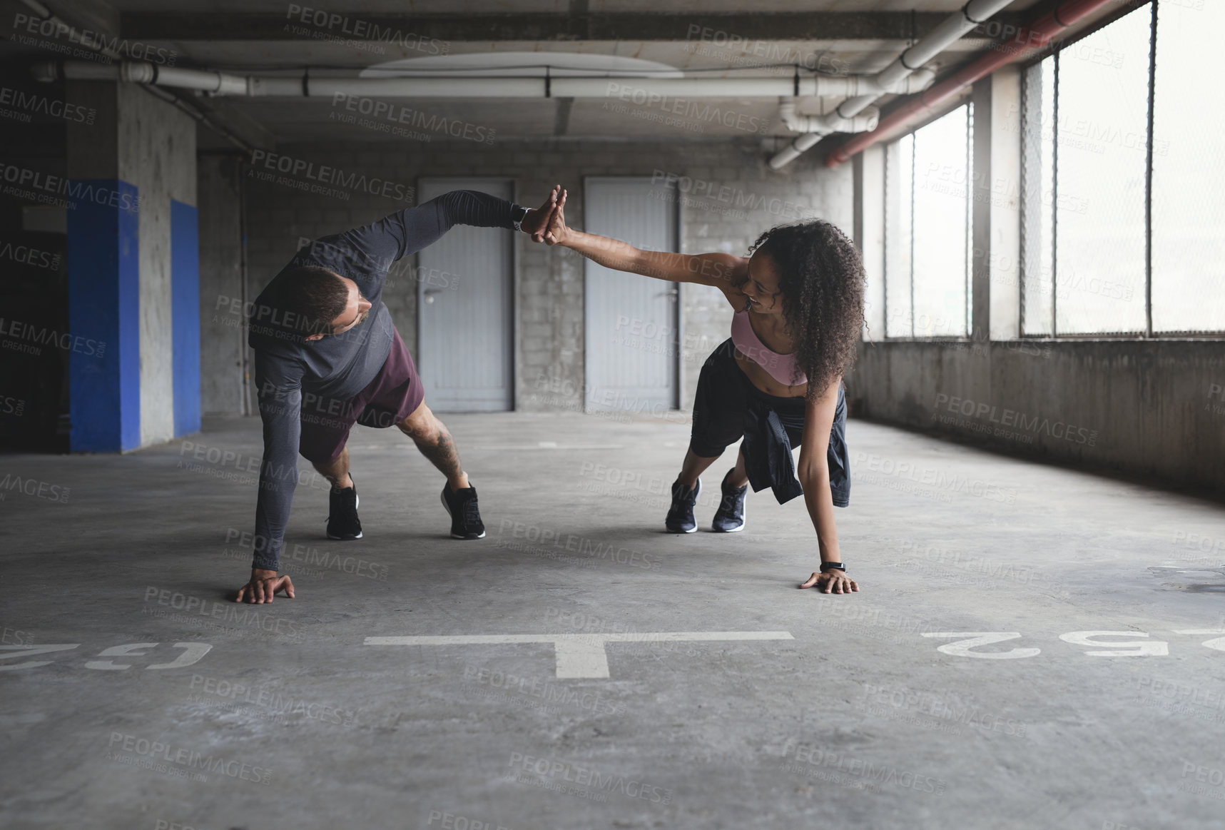 Buy stock photo Full length shot of a sporty young couple exercising together inside an underground parking lot