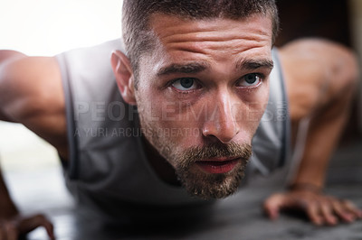 Buy stock photo Shot of a handsome young sportsman doing push ups while exercising indoors