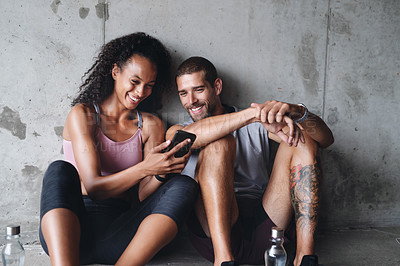 Buy stock photo Man, woman and exercise break with mobile app for fitness podcast, streaming in building for wellness. Couple, phone or workout together with rest in parking lot for health, music for gym or training