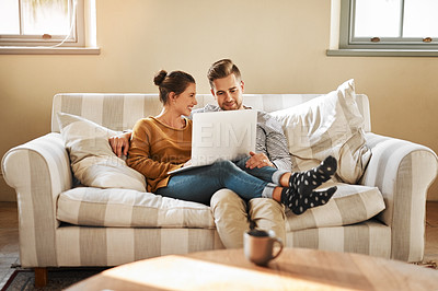 Buy stock photo Shot of a young couple using a laptop while relaxing at home