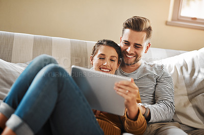 Buy stock photo Shot of a young couple using a digital tablet while relaxing at home