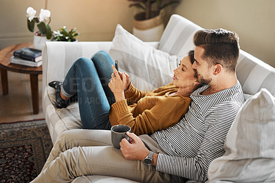 Buy stock photo Shot of a young couple using a cellphone while relaxing on the sofa at home