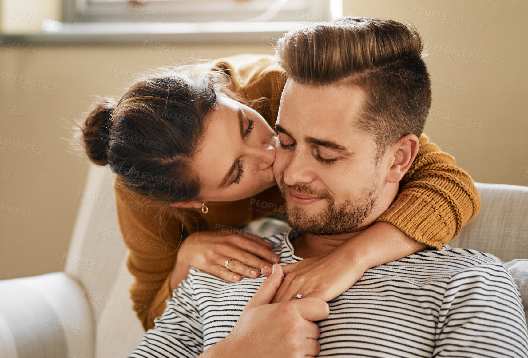 Buy stock photo Sofa, couple and hug with kiss for love, affection and bonding together in marriage at home. Happy people, woman and man with cheek embrace for admiration, commitment and connection in relationship