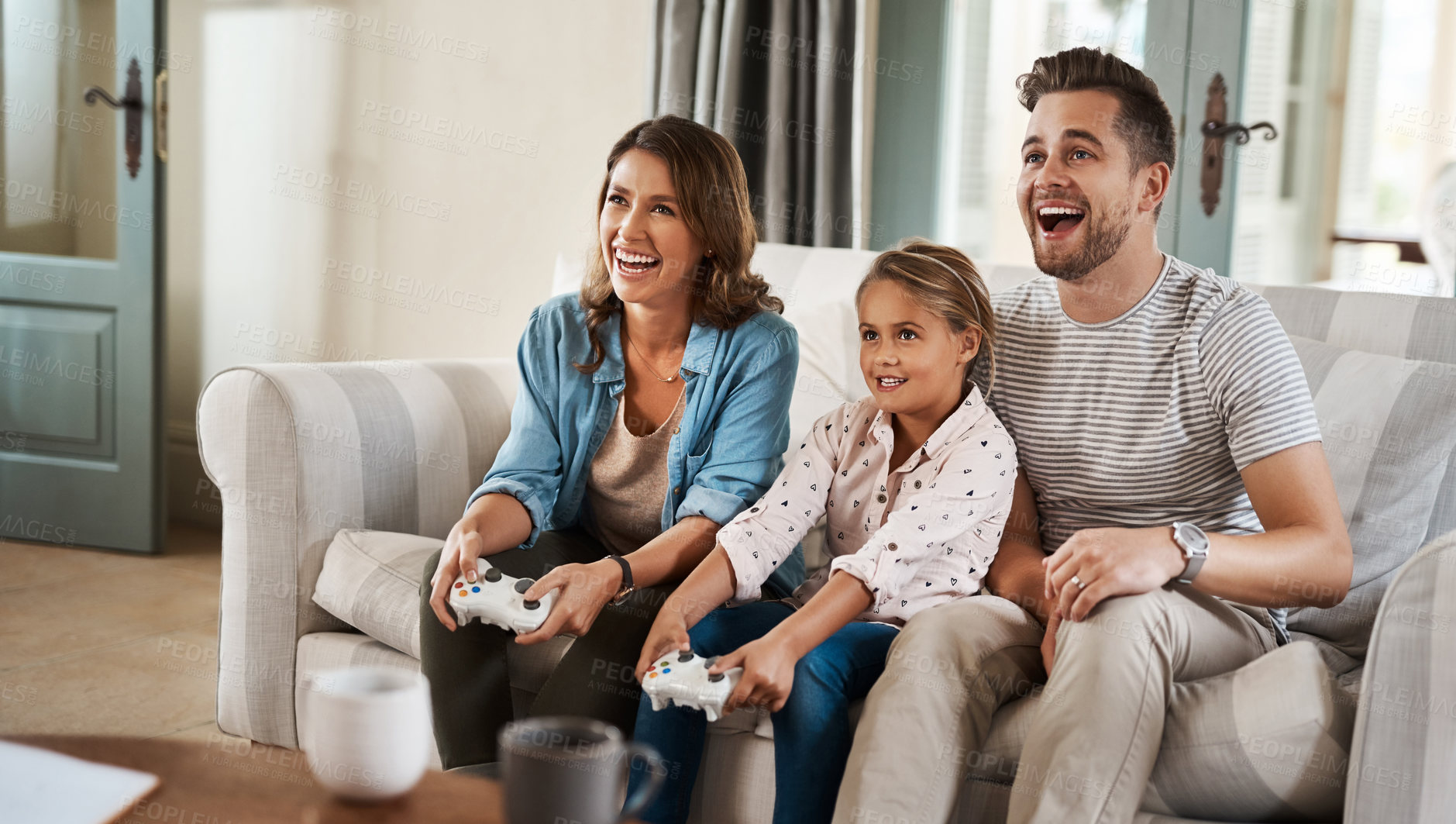 Buy stock photo Shot of a happy young family playing video games on the sofa at home