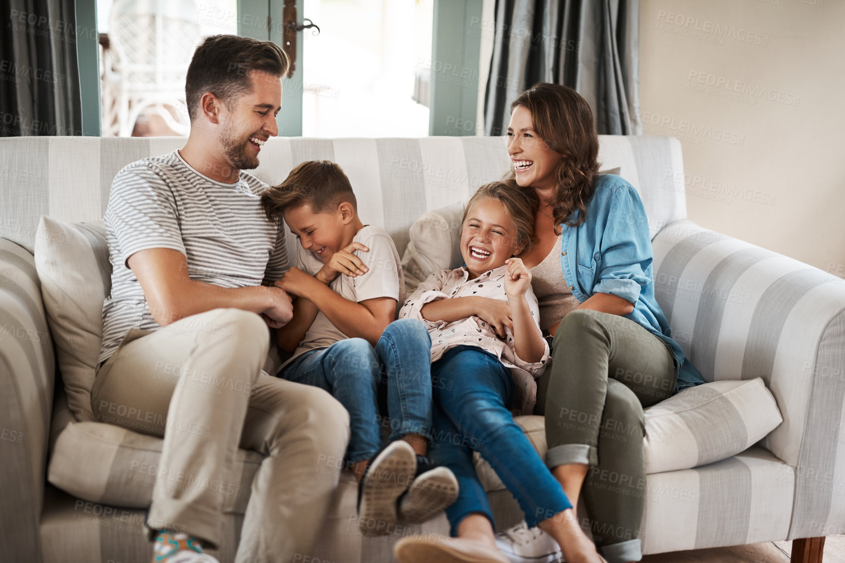 Buy stock photo Shot of a happy young family of four playing together on the sofa at home