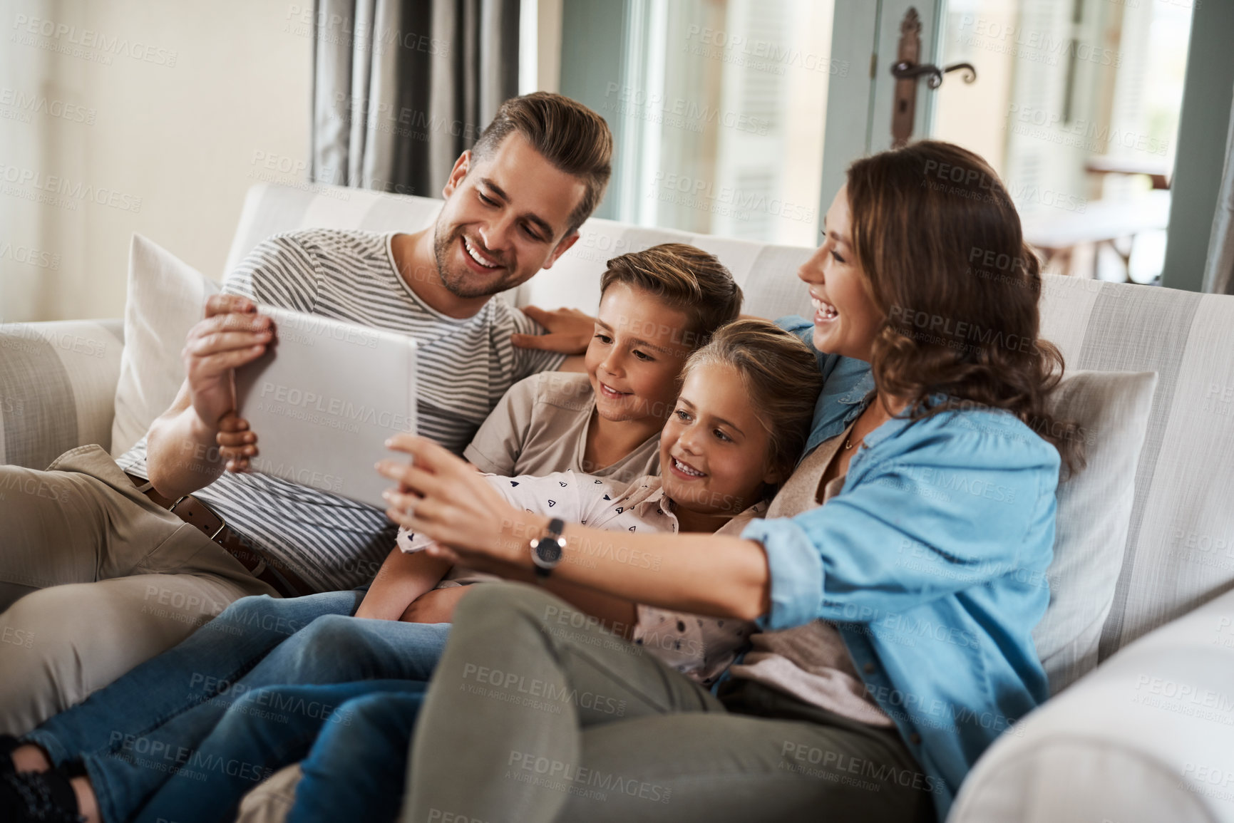 Buy stock photo Shot of a happy young family of four using a digital tablet together on the sofa at home