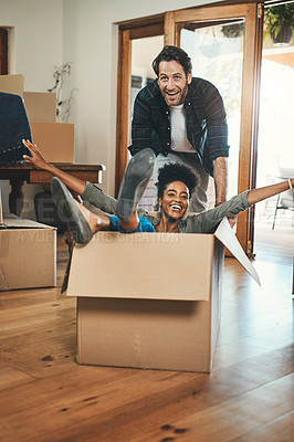 Buy stock photo Fun, playful and laughing homeowners playing in box and enjoying new home as real estate investors. Silly interracial couple and happy man pushing woman in living room of purchased property
