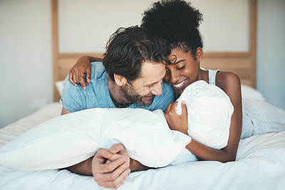 Buy stock photo Fun interracial couple laughing, bonding and lying on bed in a home bedroom and looking happy, in love and playful. Smiling man and woman hugging and cuddling after waking up in the morning together