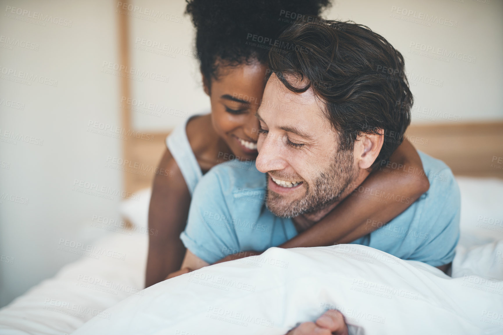 Buy stock photo Happy couple, bed and smile in hug for morning, relax or bonding relationship at home. Interracial man and woman smiling and hugging in joyful happiness for relaxing weekend together in the bedroom