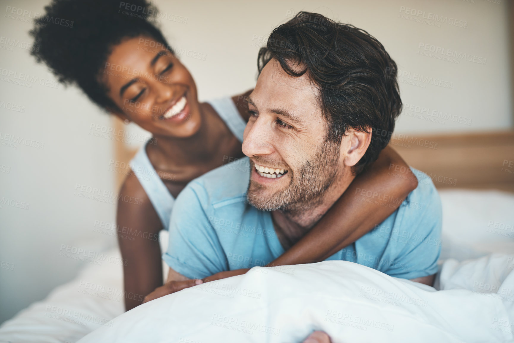Buy stock photo Happy couple, bed and hug laughing for morning, relax or bonding relationship at home. Interracial man and woman smiling, hugging and laugh in joyful happiness or relaxing weekend together in bedroom