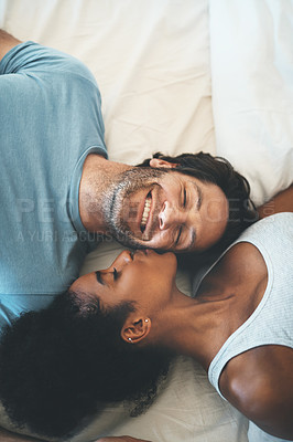 Buy stock photo Happy interracial couple, kiss and relax on bed above for morning bonding, intimate relationship or love at home. Top view of woman kissing man lying in bedroom for loving romance, care or affection
