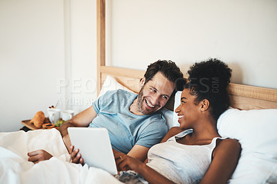 Buy stock photo Happy couple, tablet and laughing on bed for joke, funny entertainment or online streaming at home. Interracial man and woman person on technology in relax for morning or social media in the bedroom