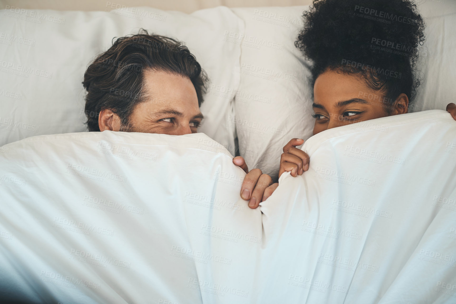 Buy stock photo Intimate, loving and affectionate couple or lovers in bed after a passionate night or sensual sex. Playful interracial partners having fun or hiding under blanket on a romantic honeymoon.