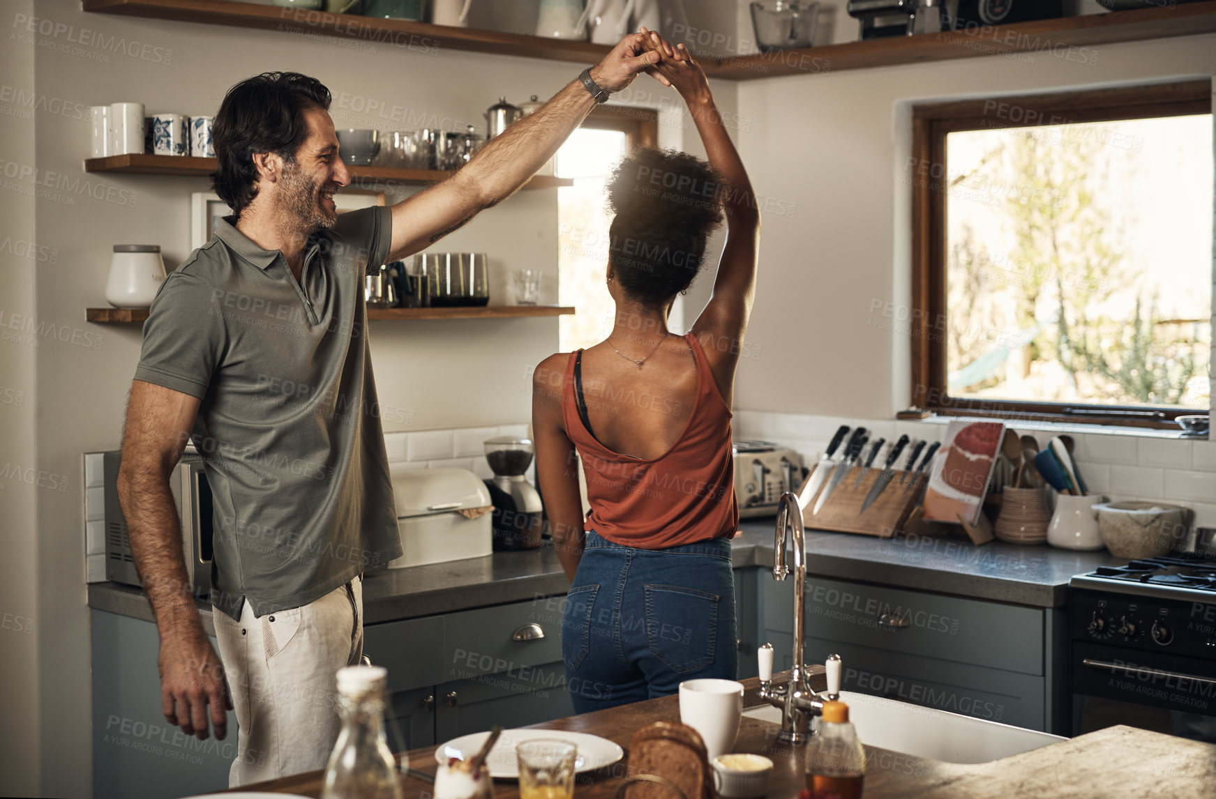 Buy stock photo Happy, romantic and interracial couple dancing and having fun while bonding in kitchen at home. Carefree and energetic loving couple feeling cheerful while sharing a dance and enjoying time together