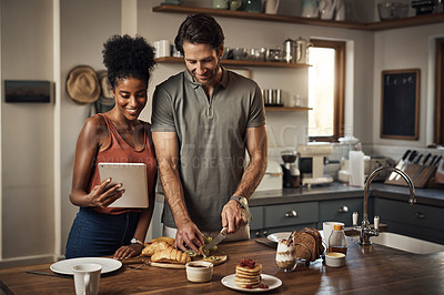 Buy stock photo Couple cooking breakfast with a tablet while searching for online recipes and videos on the internet. Happy interracial lovers preparing a healthy meal in their home kitchen while browsing online
