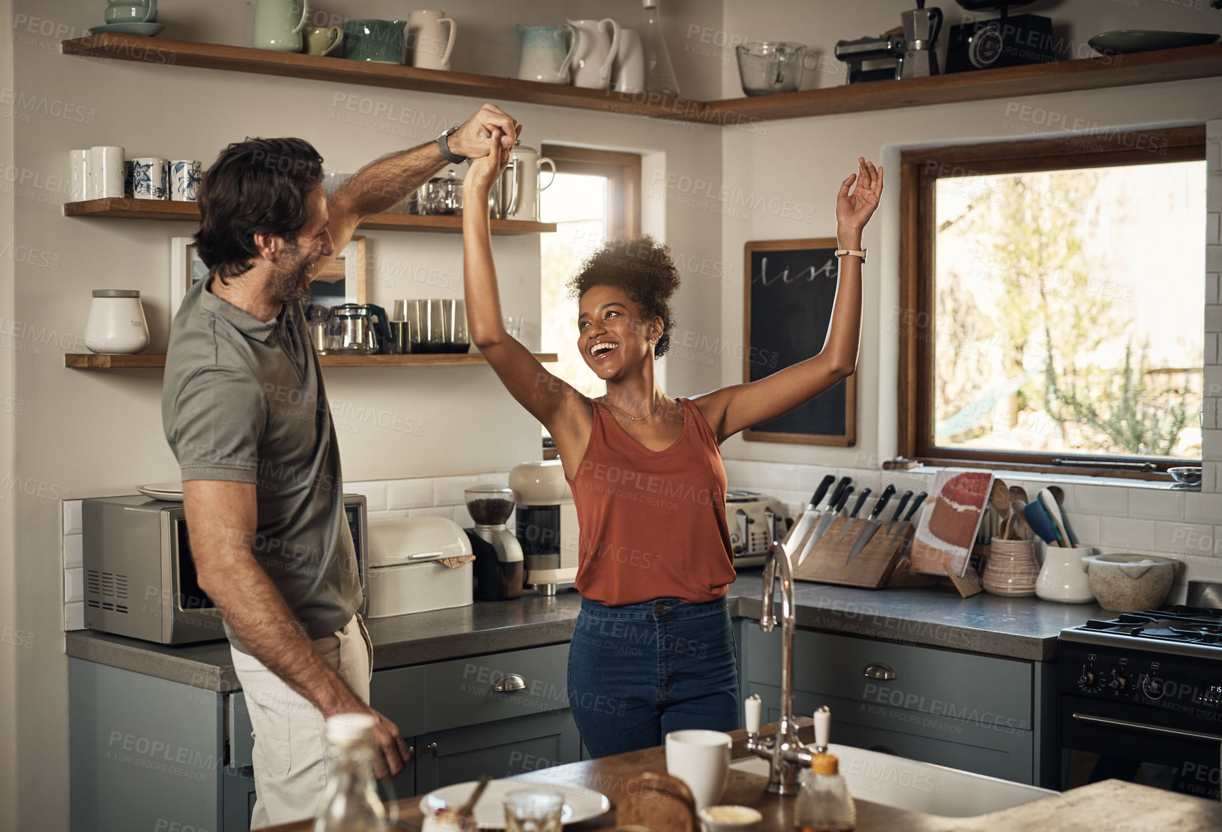 Buy stock photo Happy interracial couple dancing, having fun and bonding together in the kitchen at home. Carefree, cheerful and loving husband and wife being playful, doing a dance and enjoying a romantic day