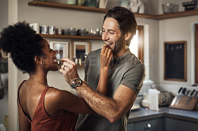 Buy stock photo Cropped shot of an affectionate young couple feeding each other fruit in their kitchen at home