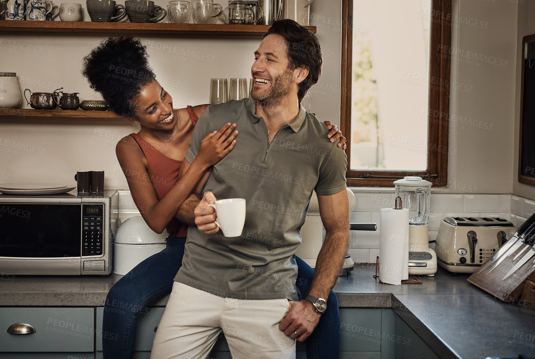 Buy stock photo Interracial couple, together and happiness with tea in kitchen for wellness, morning routine or bonding in home. Man, woman and smile in house with coffee for health, relax with partner or care