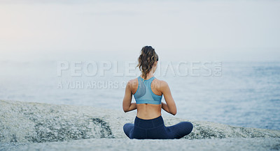 Buy stock photo Rearview shot of an unrecognizable woman sitting cross legged and meditating alone by the ocean during an overcast day