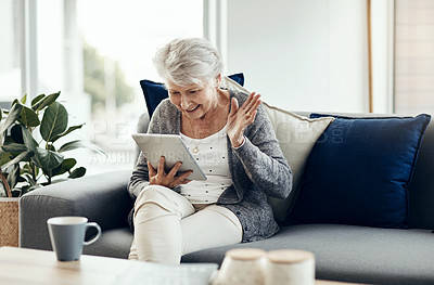 Buy stock photo Shot of a senior woman using a digital tablet while relaxing at home