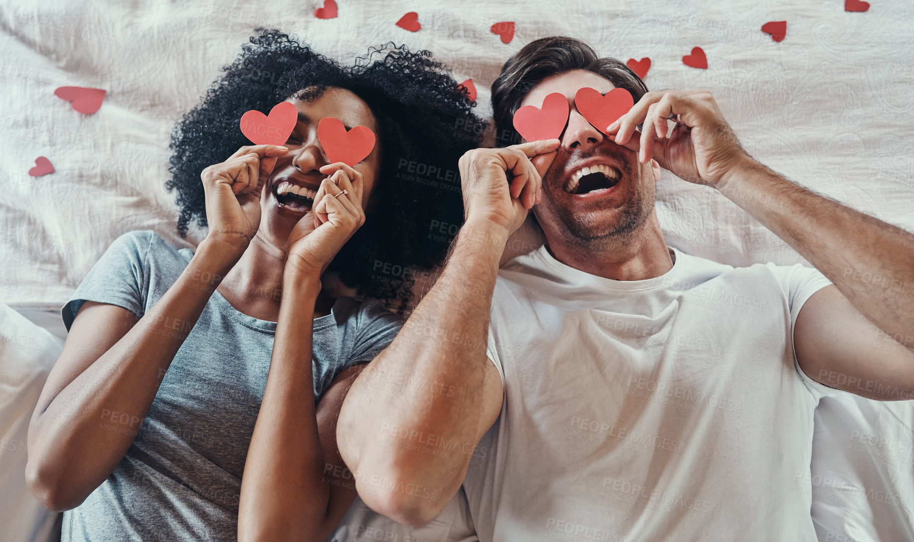 Buy stock photo High angle shot of a young couple covering their faces with heart shaped decorations in their bedroom at home