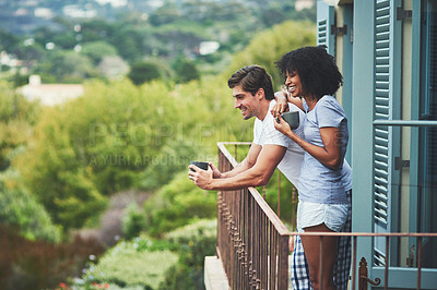 Buy stock photo Shot of an affectionate young couple drinking coffee and looking at the view while standing on a balcony at home