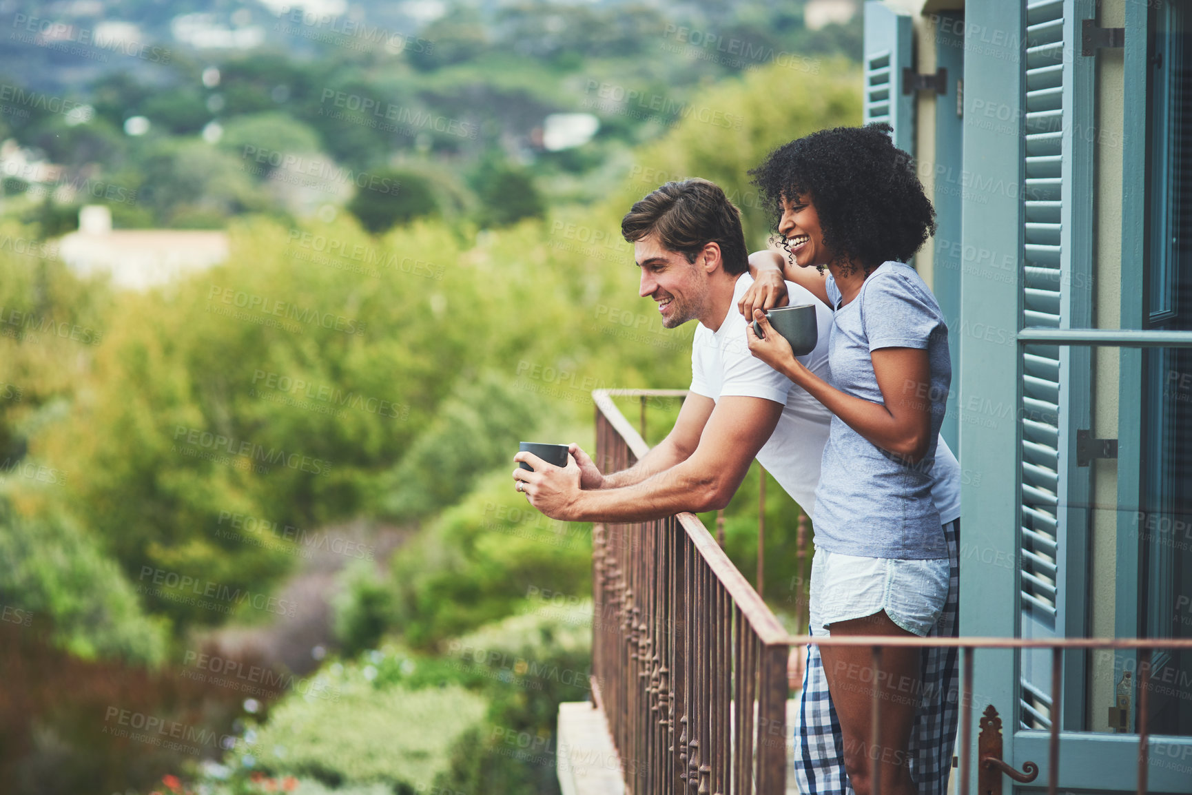 Buy stock photo Shot of an affectionate young couple drinking coffee and looking at the view while standing on a balcony at home