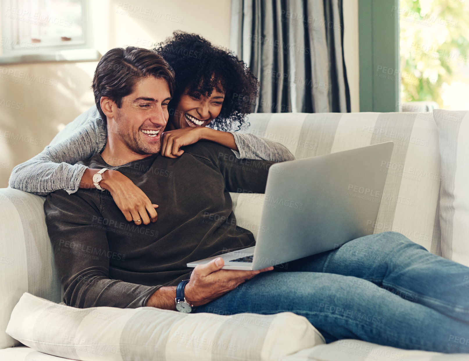 Buy stock photo Shot of an affectionate young couple using a laptop together while relaxing in their living room at home