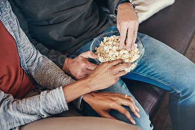 Buy stock photo Shot of an unrecognizable couple eating popcorn together while sitting on a sofa at home