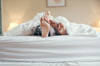 Buy stock photo Shot of an unrecognizable couple's feet poking out under the sheets while lying in bed together at home