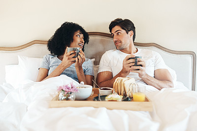 Buy stock photo Shot of an affectionate young couple having breakfast in bed together at home