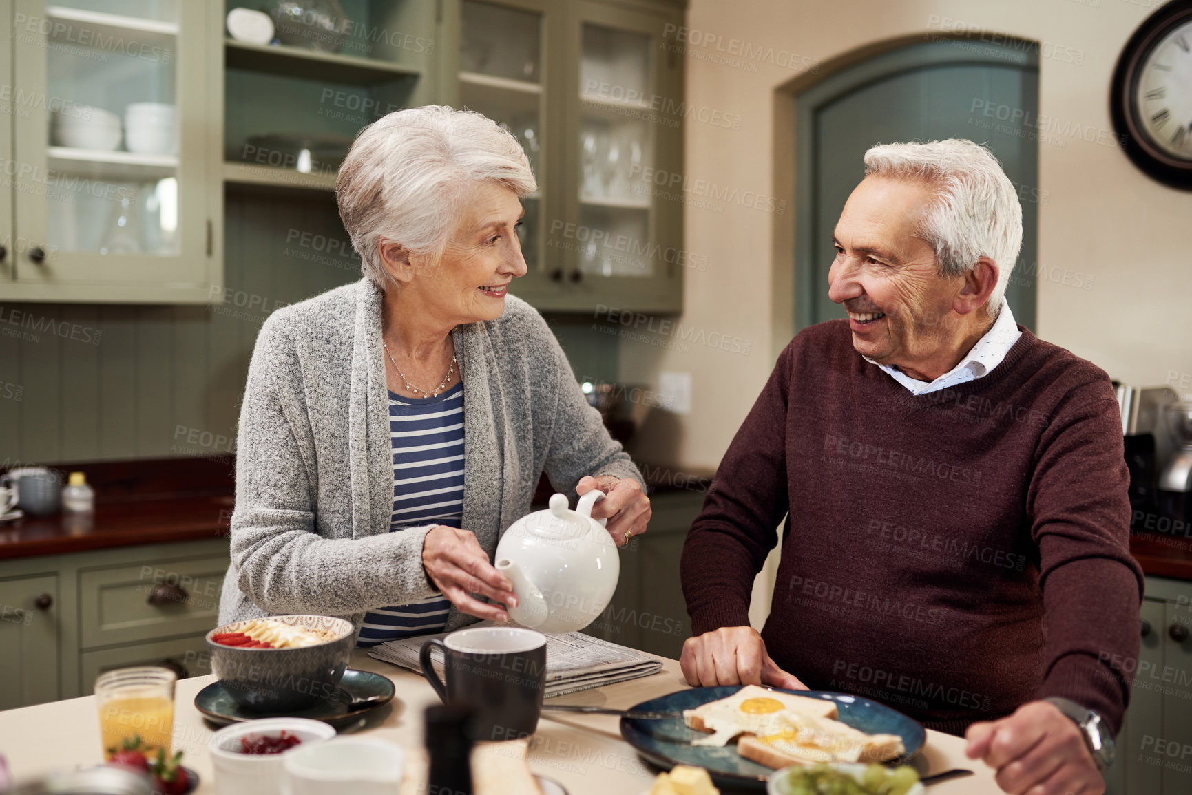 Buy stock photo Shot of an affectionate senior couple drinking tea and having a meal together in the kitchen at home