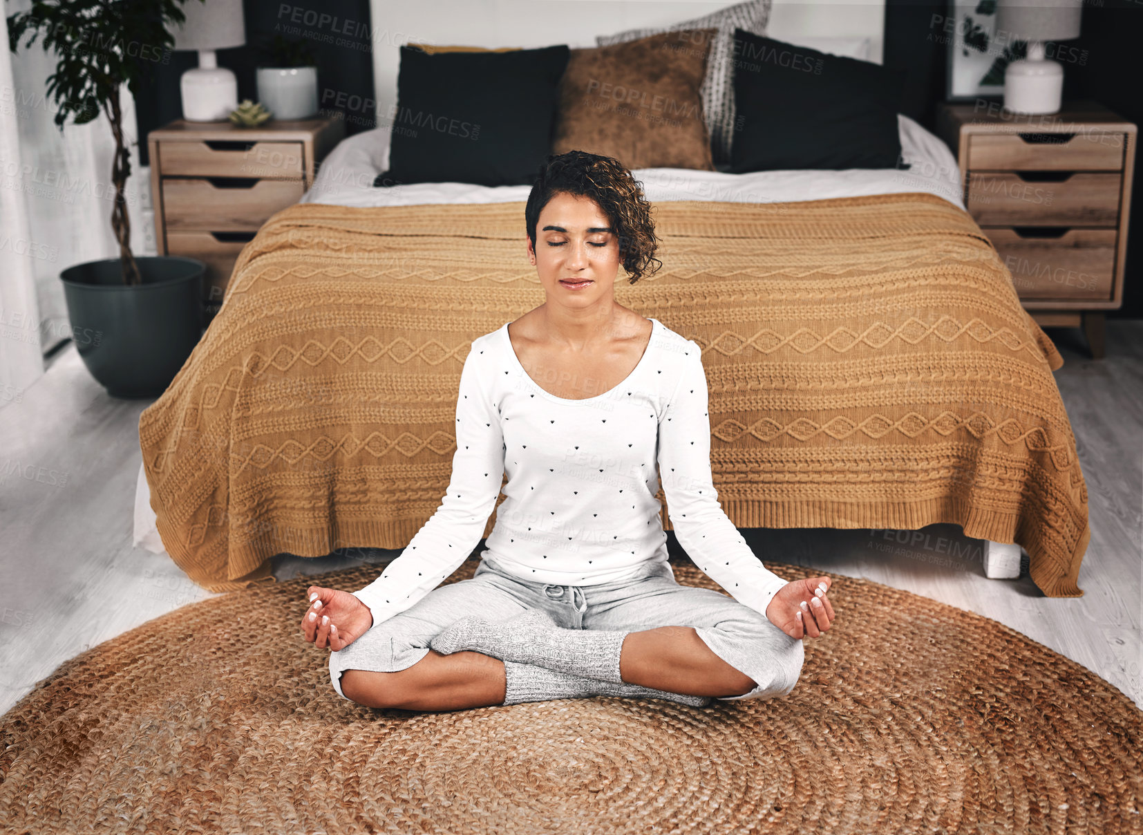 Buy stock photo Cropped shot of an attractive young woman sitting and meditating by the foot of her bed in her bedroom