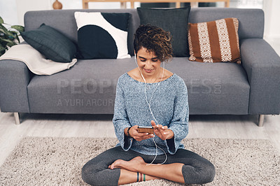 Buy stock photo Full length shot of an attractive young woman sitting in her living room and listening to music through her cellphone